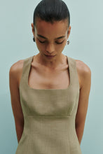A close-up lifestyle view shows a model wearing the Nude Lucy Thea Top in moss with a square neckline and fitted shape.
