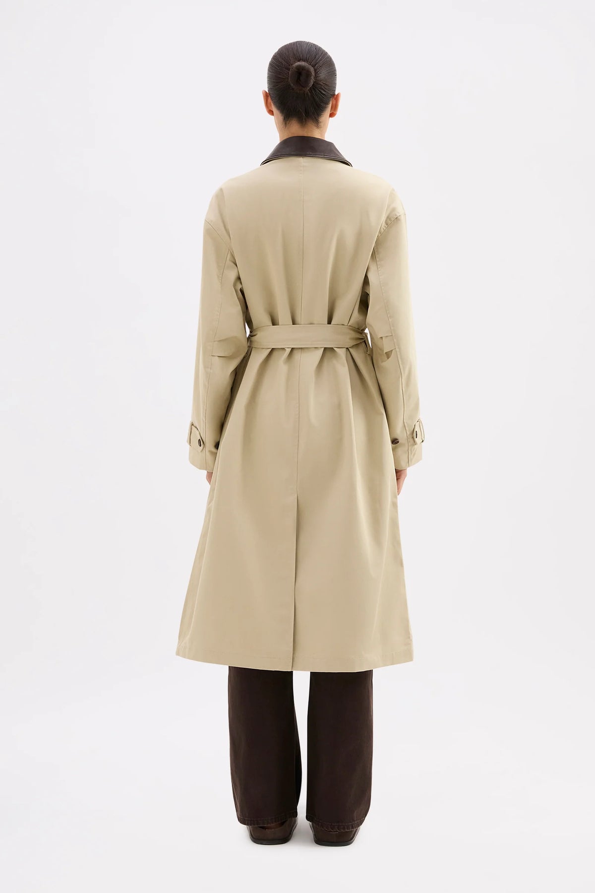 Person wearing a beige trench coat on a white background