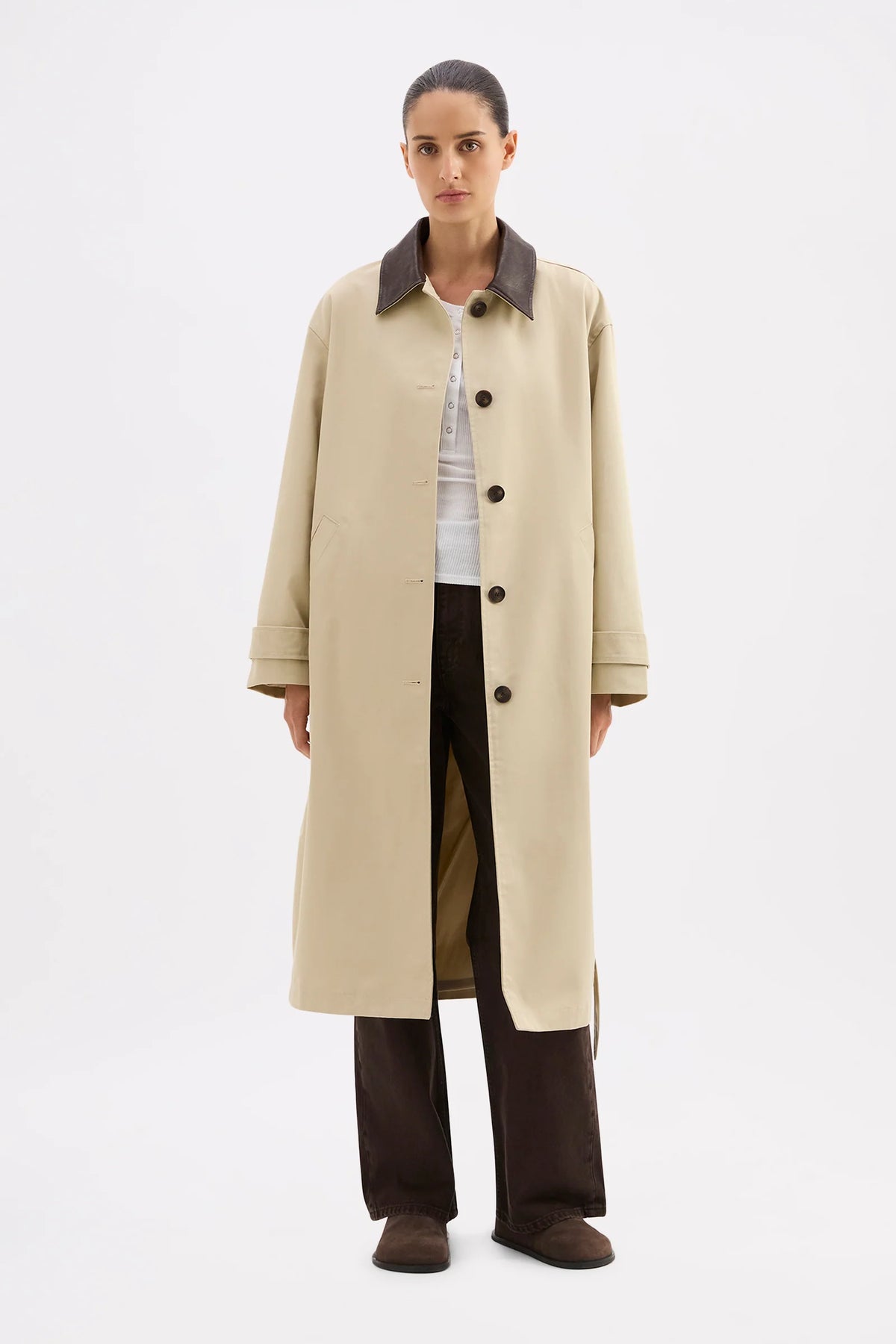 Person wearing a beige trench coat with dark collar and buttons on a white background