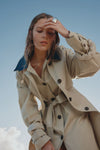 Woman wearing a beige trench coat against a clear blue sky.