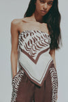A model wears the Vela print scarf as a strapless top, featuring a brown and cream abstract pattern and a pointed front.