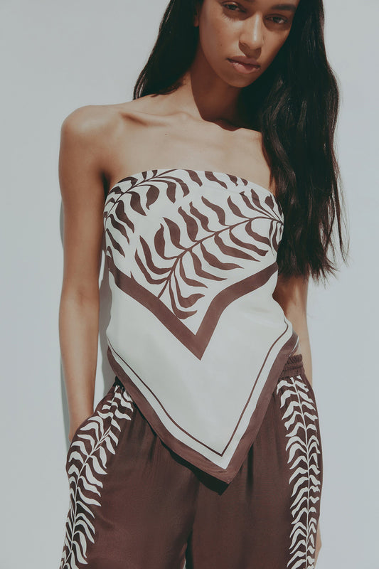 A model wears the Vela print scarf as a strapless top, featuring a brown and cream abstract pattern and a pointed front.