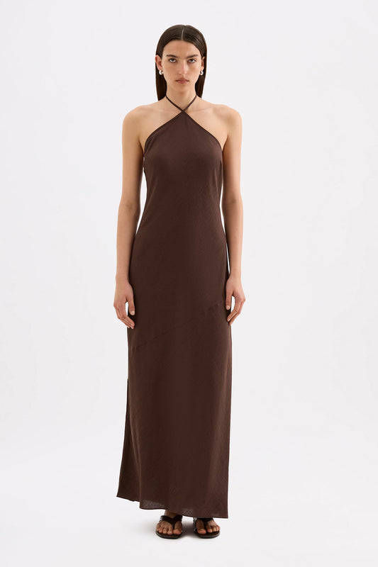 A model wears a chocolate brown maxi dress with a halter neckline and relaxed silhouette in a full front studio view.