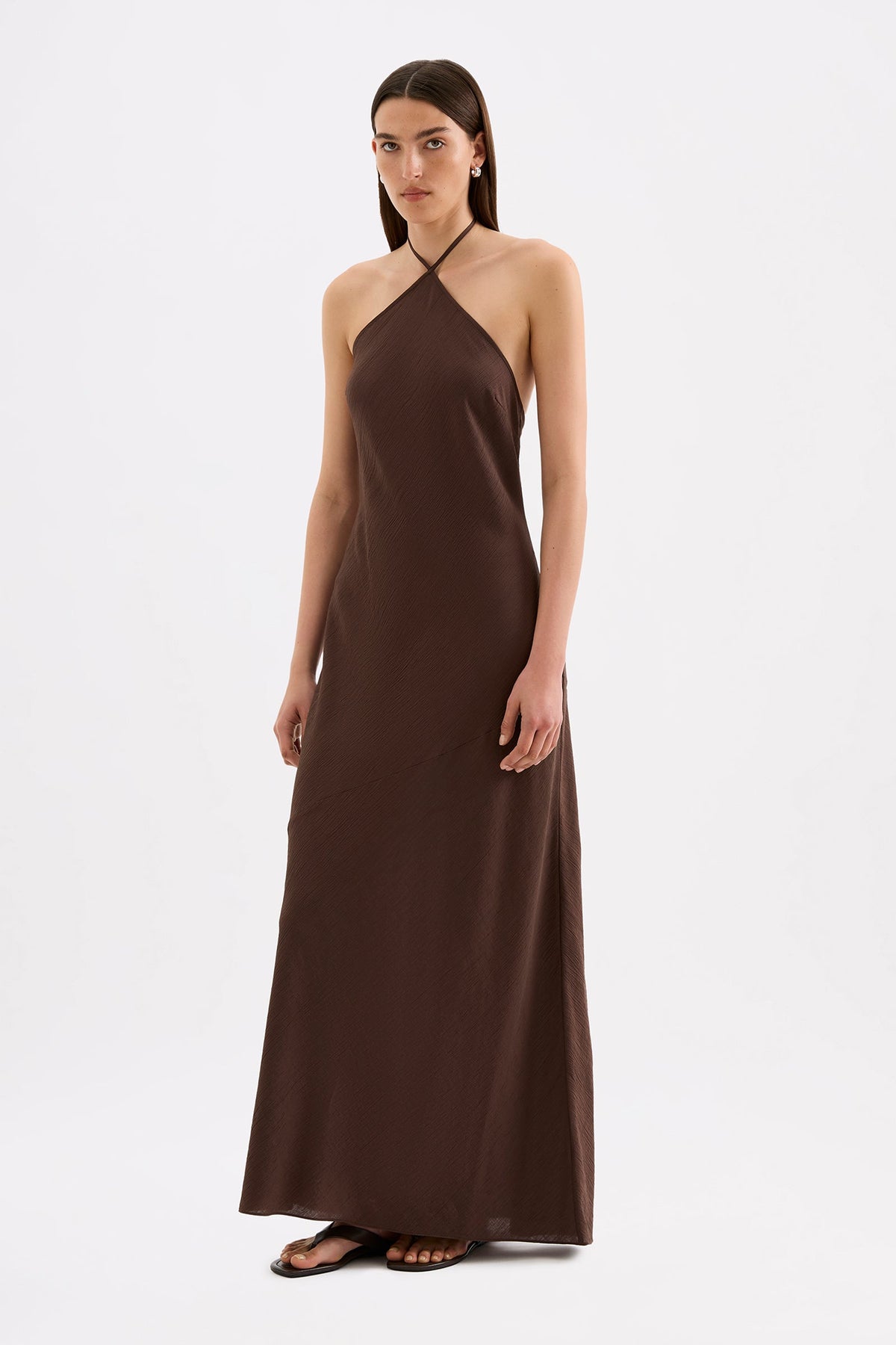 The model wears the chocolate brown maxi dress in a three-quarter side view, showing the halter neckline and long flowing silhouette.