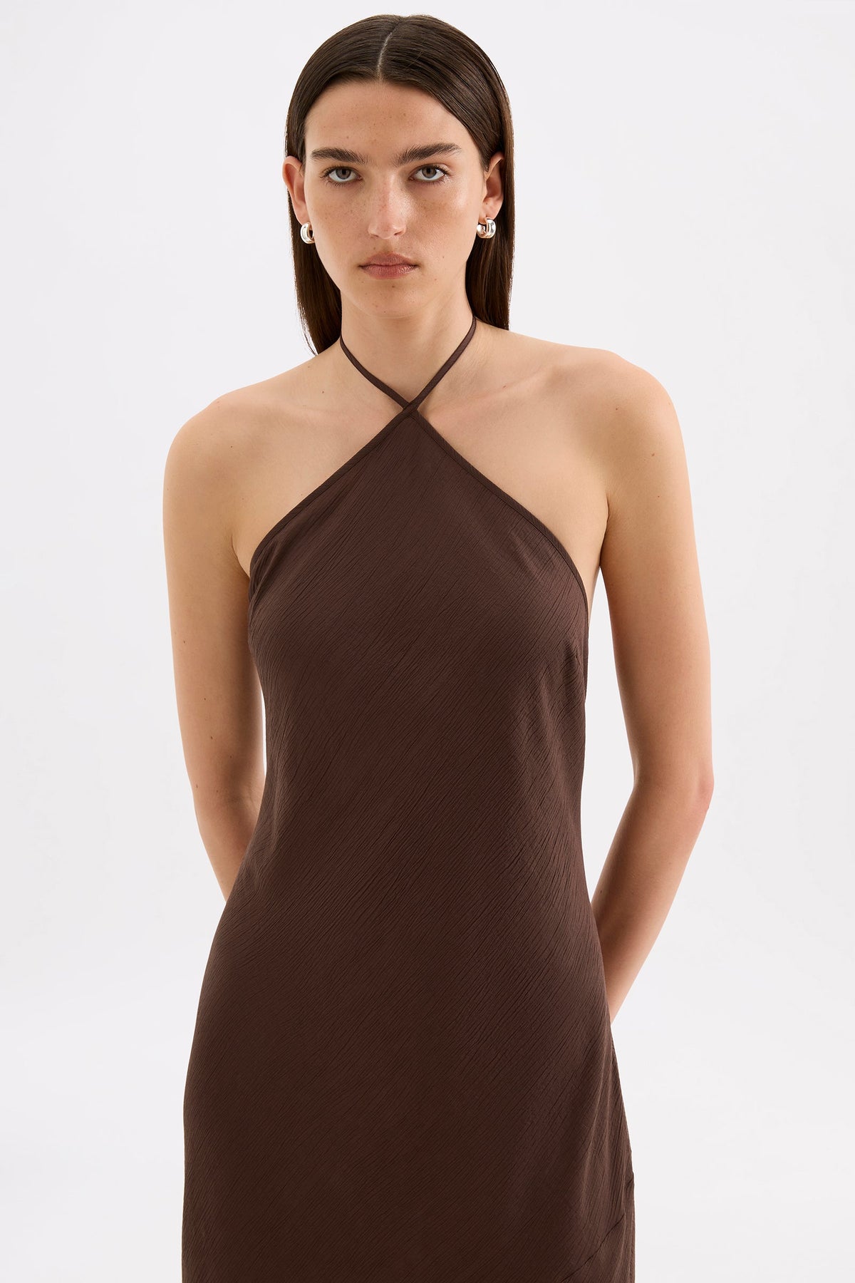 Close-up front view of the chocolate brown maxi dress showing the halter neckline and asymmetric seam through the body.