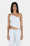 A model wearing a pale blue asymmetrical top with a diagonal neckline, thin halterneck straps and an angled hem, shown from the front in a close view.