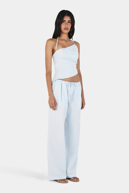  A model wearing a pale blue asymmetrical halterneck top with a fitted shape and diagonal hem, paired with matching wide-leg drawstring trousers in a full-length front three-quarter view.