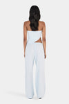 A rear view of a model wearing a pale blue top with a wrapped asymmetrical back, slim halterneck straps and an angled hem, paired with matching wide-leg trousers.