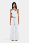 A front view of a model wearing a pale blue asymmetrical halterneck top with a slanted neckline and angled hem, paired with matching full-length wide-leg trousers.