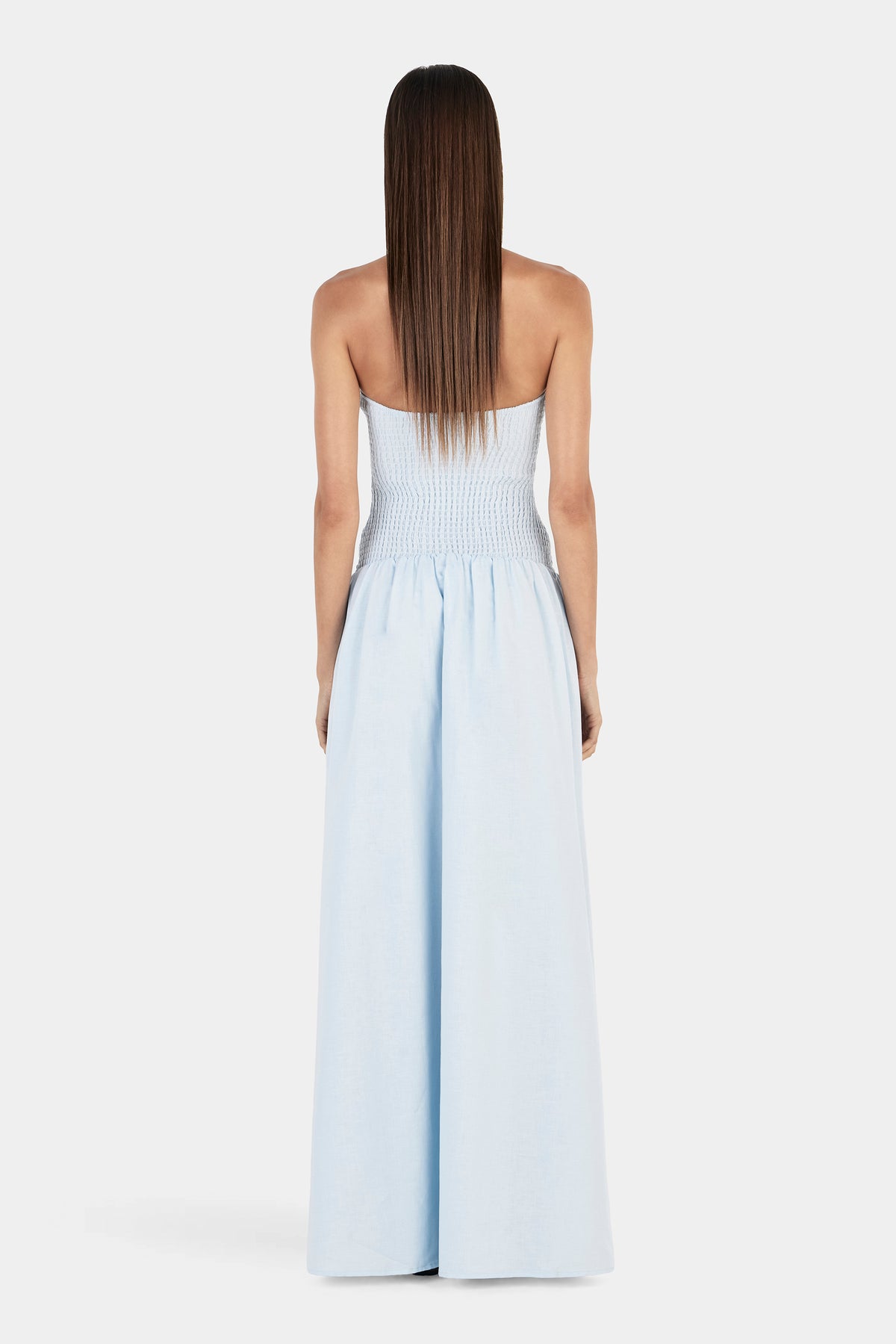 A full rear view of the cornflower blue dress showing the shirred back bodice and long, flowing skirt.