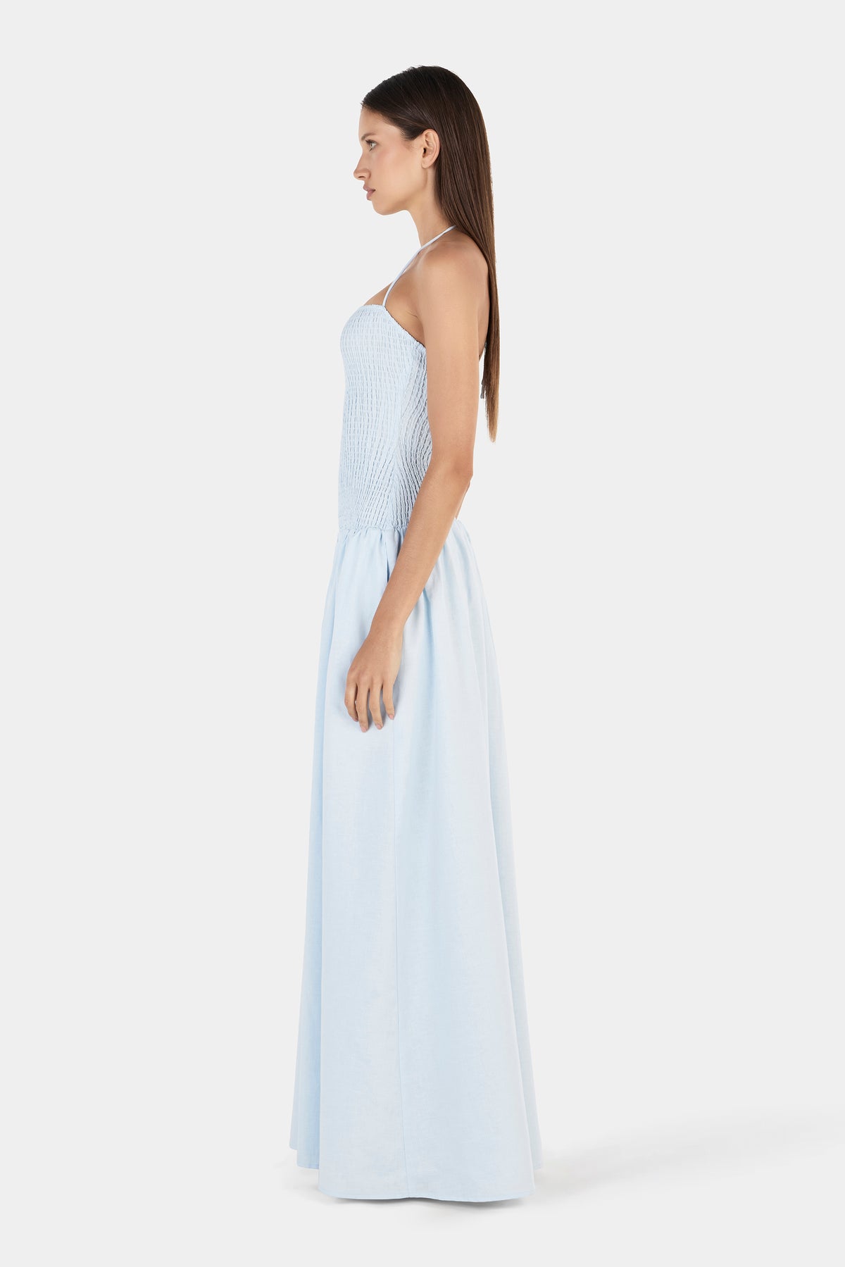 A side view of a cornflower blue maxi dress with a shirred bodice, thin halter strap and flowing full-length skirt.