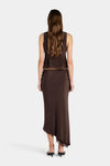 Rear view of a model wearing a chocolate brown midi skirt, showing the smooth back, fitted waist, straight drape through the body and asymmetrical hem finished with dark lace trim.