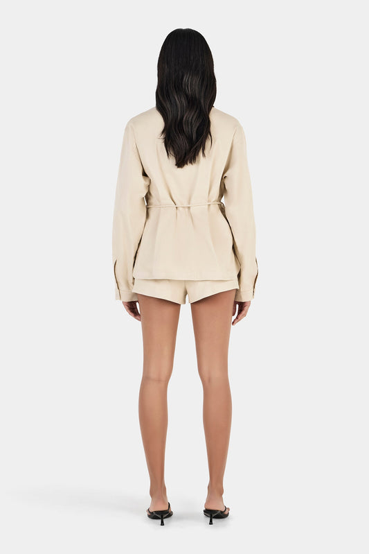 Model wearing the beige jacket with matching shorts, showing the oversized fit, waist tie and clean back silhouette, full-length back view
