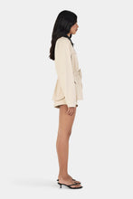 Model wearing the beige jacket with matching shorts and black heels, showing the contrast collar, relaxed sleeves and cinched waist, full-length side view
