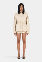 Model wearing the beige jacket with matching shorts, showing the contrast collar, waist tie and relaxed long sleeves, full-length front view
