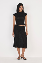 Model wearing the black Midi Skirt with a matching fitted top and black heeled sandals, showing the flowing midi length, lightweight crinkled texture, clean waistband and softly draped silhouette in a full-length front view.