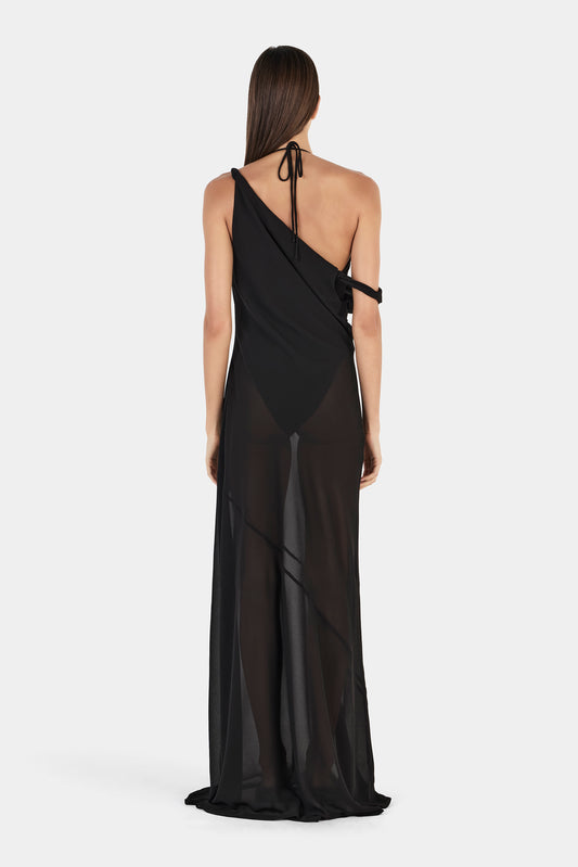 A rear view of a black maxi dress featuring a halter tie at the neck, an open back, an asymmetrical bodice and a sheer full-length skirt.