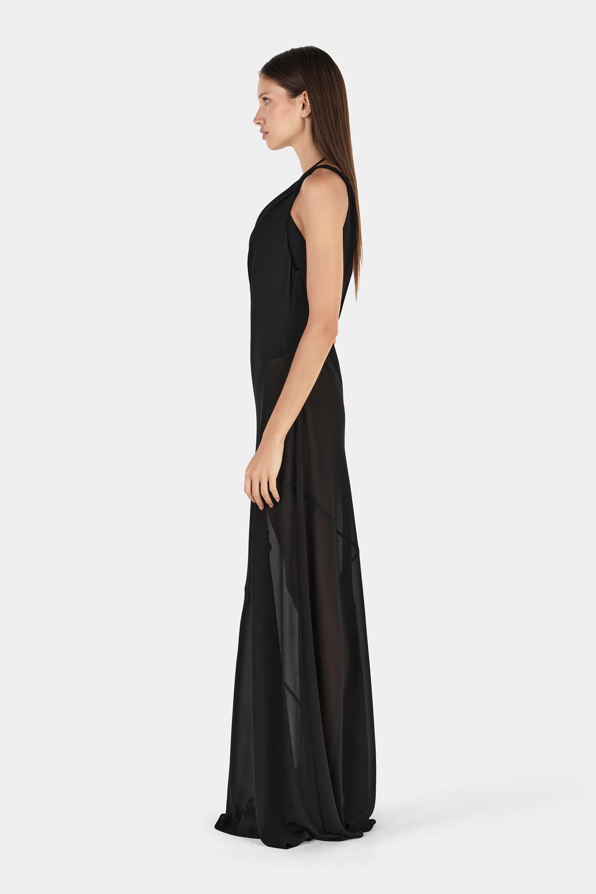 A side profile of a black maxi dress with a sleek fitted upper section and a sheer floor-length skirt that falls close to the body.