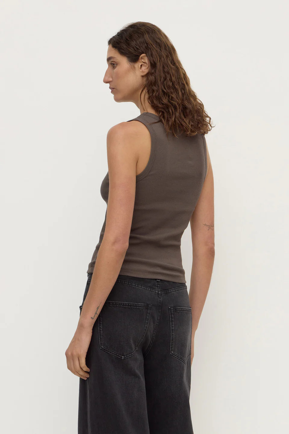 Model wearing the bark rib tank with washed black jeans, showing the fitted shape, sleeveless cut and clean scoop-back silhouette, back angled view
