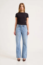 Model wearing the Surrender mid-blue boyfriend jeans with a fitted black tee and brown pointed heels, showing the mid-rise waist, relaxed fit and straight full-length legs in a front view.