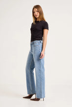 Model wearing the Surrender jeans with a fitted black tee and brown pointed heels, showing the mid-rise waist, front scoop pockets and relaxed straight-leg shape in an angled side view.