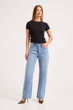 Model wearing the mid-blue boyfriend jeans with a fitted black tee and pointed heels, showing the button fly, five-pocket styling, relaxed thigh and straight-leg silhouette in a full-length front view.