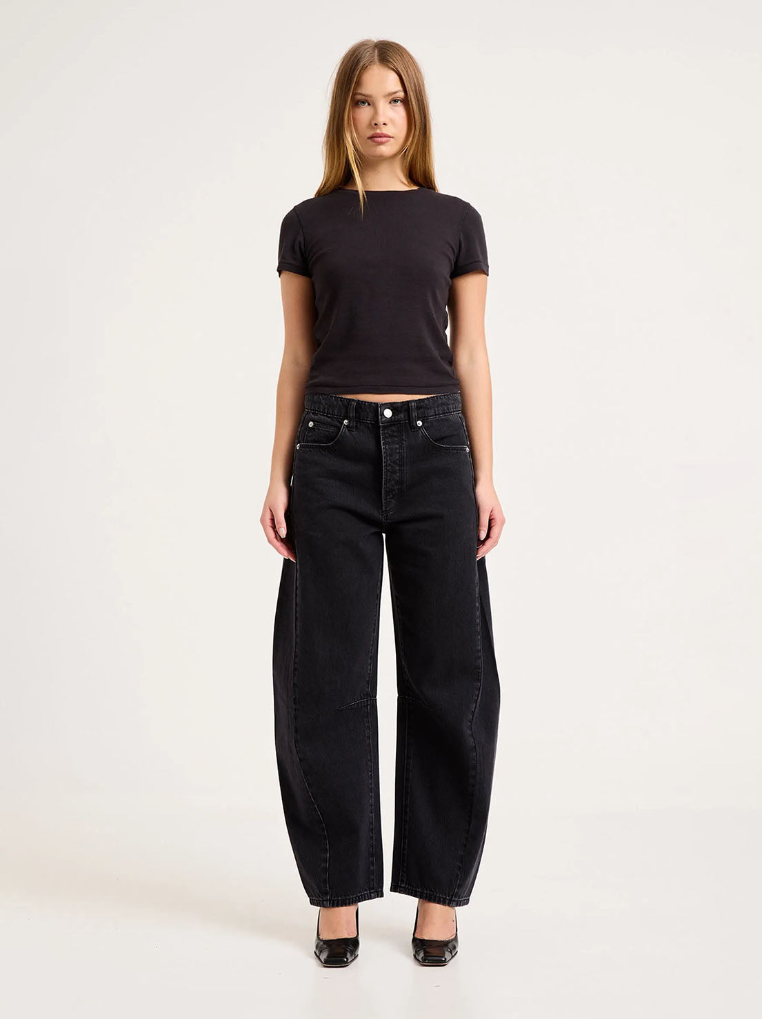 Model wearing the washed black barrel jeans with a fitted black tee and black heels, showing the mid-rise waist, five-pocket styling, knee darts and sculpted leg shape in a full-length front view.