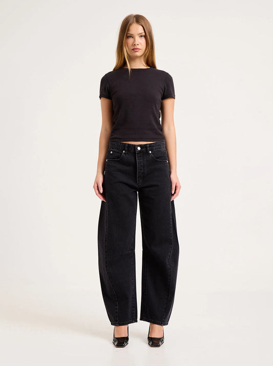 Model wearing the washed black barrel jeans with a fitted black tee and black heels, showing the mid-rise waist, five-pocket styling, knee darts and sculpted leg shape in a full-length front view.