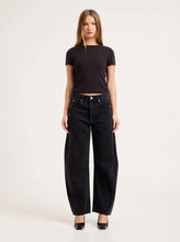 Model wearing the washed black barrel jeans with a fitted black tee and black heels, showing the mid-rise waist, five-pocket styling, knee darts and sculpted leg shape in a full-length front view.