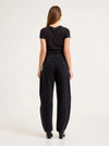 Model wearing the black barrel jeans with a fitted black tee, showing the back yoke, square rear pockets, relaxed seat and tapered ankle-length legs in a full-length back view.