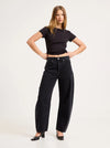 Model wearing the Mercer Black jeans with a cropped black tee and heels, showing the silver button, front pockets, side panels and curved barrel-leg shape in a styled front view.
