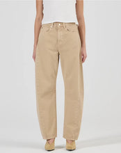 A model wears the Rolla’s Arc Barrel Long Jean in Dune with a white fitted top in a front studio view.
