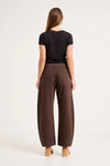 A rear view shows the chocolate-brown pants with square back pockets, belt loops, visible stitching and a relaxed barrel-leg shape.