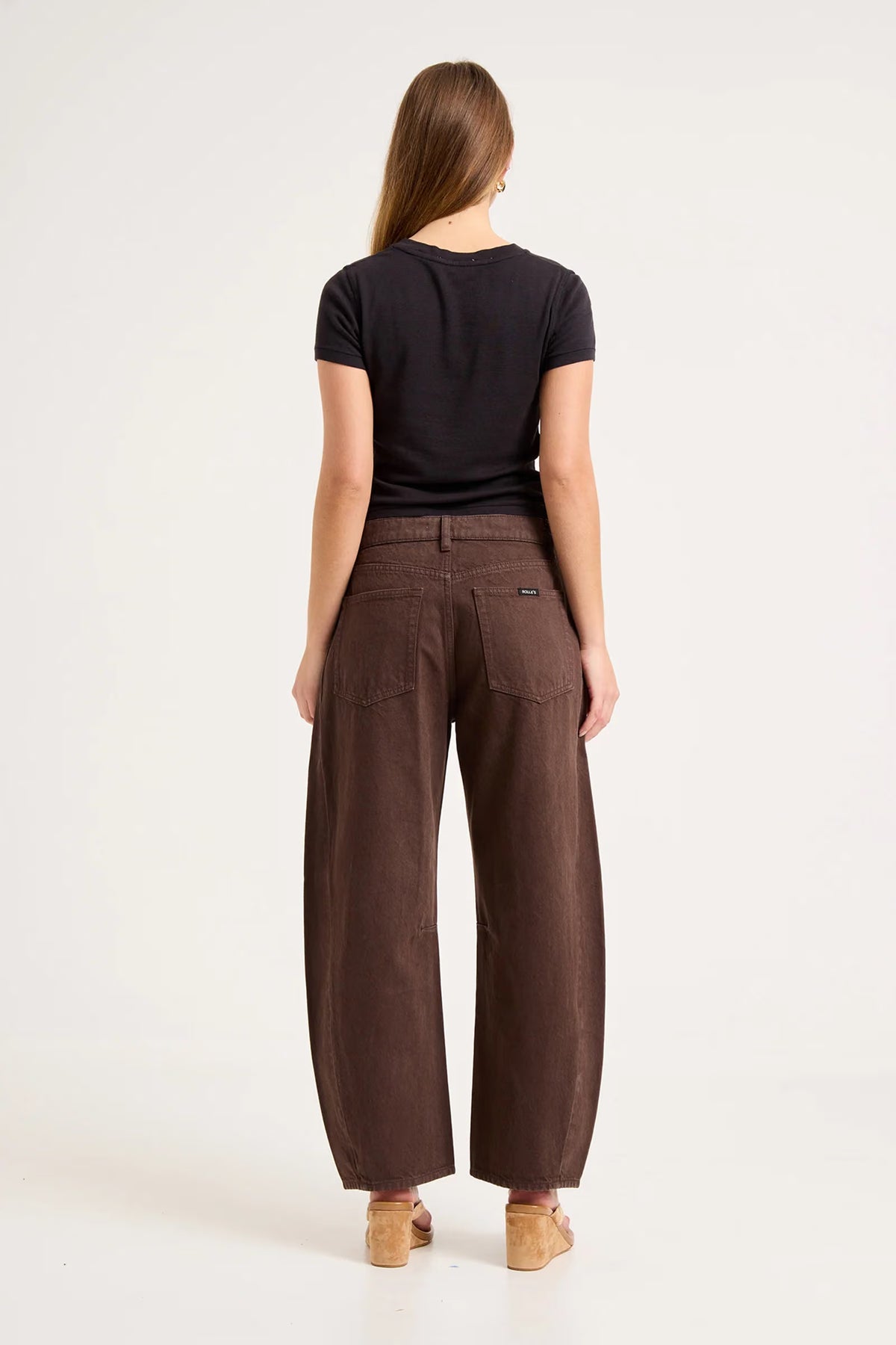 A rear view shows the chocolate-brown pants with square back pockets, belt loops, visible stitching and a relaxed barrel-leg shape.