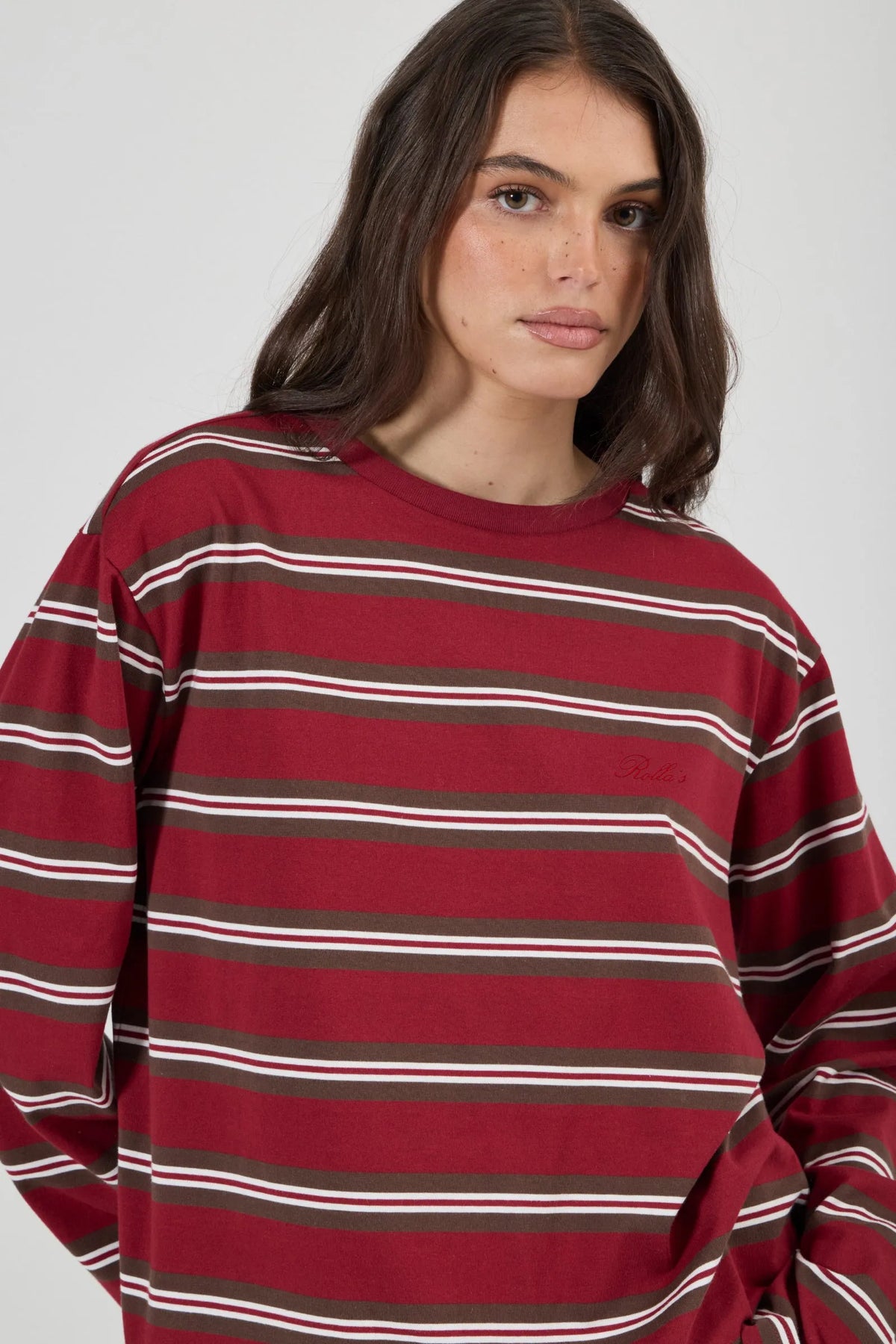 Close-up of the burgundy striped long-sleeve tee, showing the crew neckline, horizontal brown and white stripes, dropped shoulders and subtle tonal script embroidery at the chest.