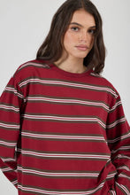 Close-up of the burgundy striped long-sleeve tee, showing the crew neckline, horizontal brown and white stripes, dropped shoulders and subtle tonal script embroidery at the chest.