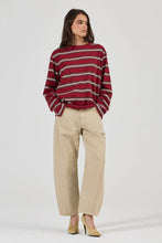 Model wearing the burgundy striped long-sleeve tee with beige relaxed jeans and tan heels, showing the crew neckline, oversized sleeves and loose drape through the body in a full-length front view.
