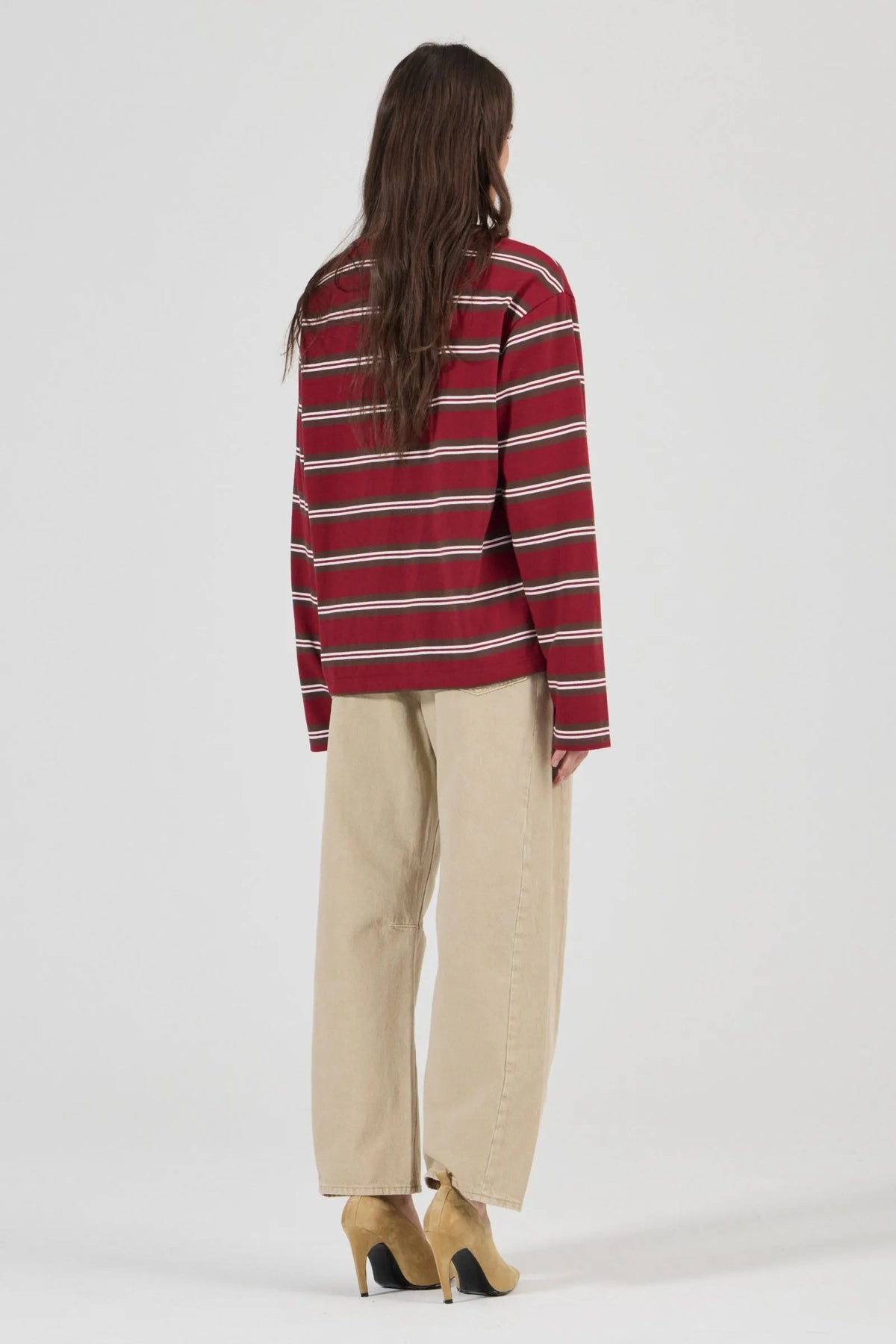 Model wearing the burgundy striped long-sleeve tee with beige jeans and tan heels, showing the dropped shoulders, straight back, long sleeves and relaxed fit in a full-length back view.