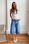 Woman wearing mid-blue denim culottes with a light blue fitted top and pointed heels in an indoor setting.