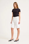 Woman wearing white knee-length denim shorts with a black fitted T-shirt and black heeled shoes in a studio setting.
