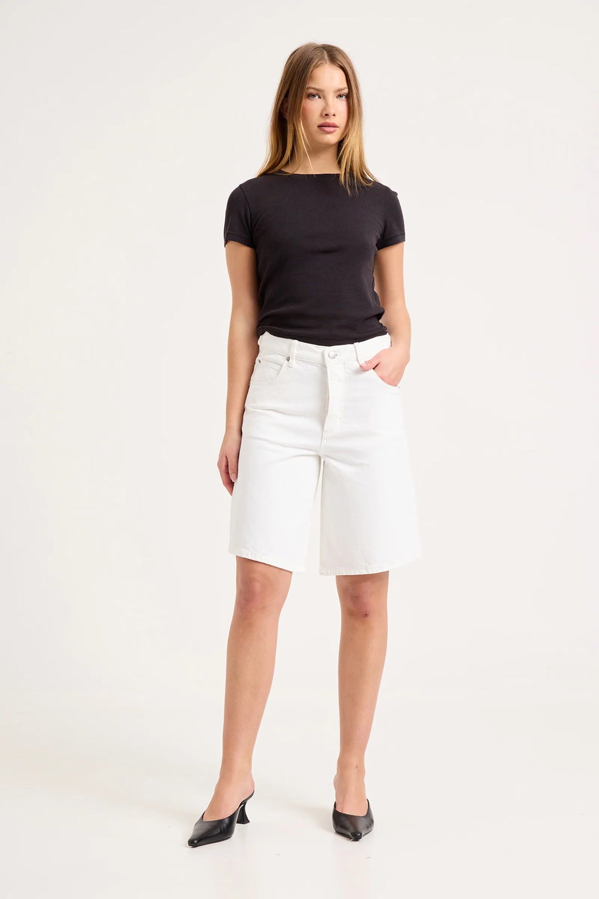 Woman wearing white knee-length denim shorts with a black fitted T-shirt, shown from the front.