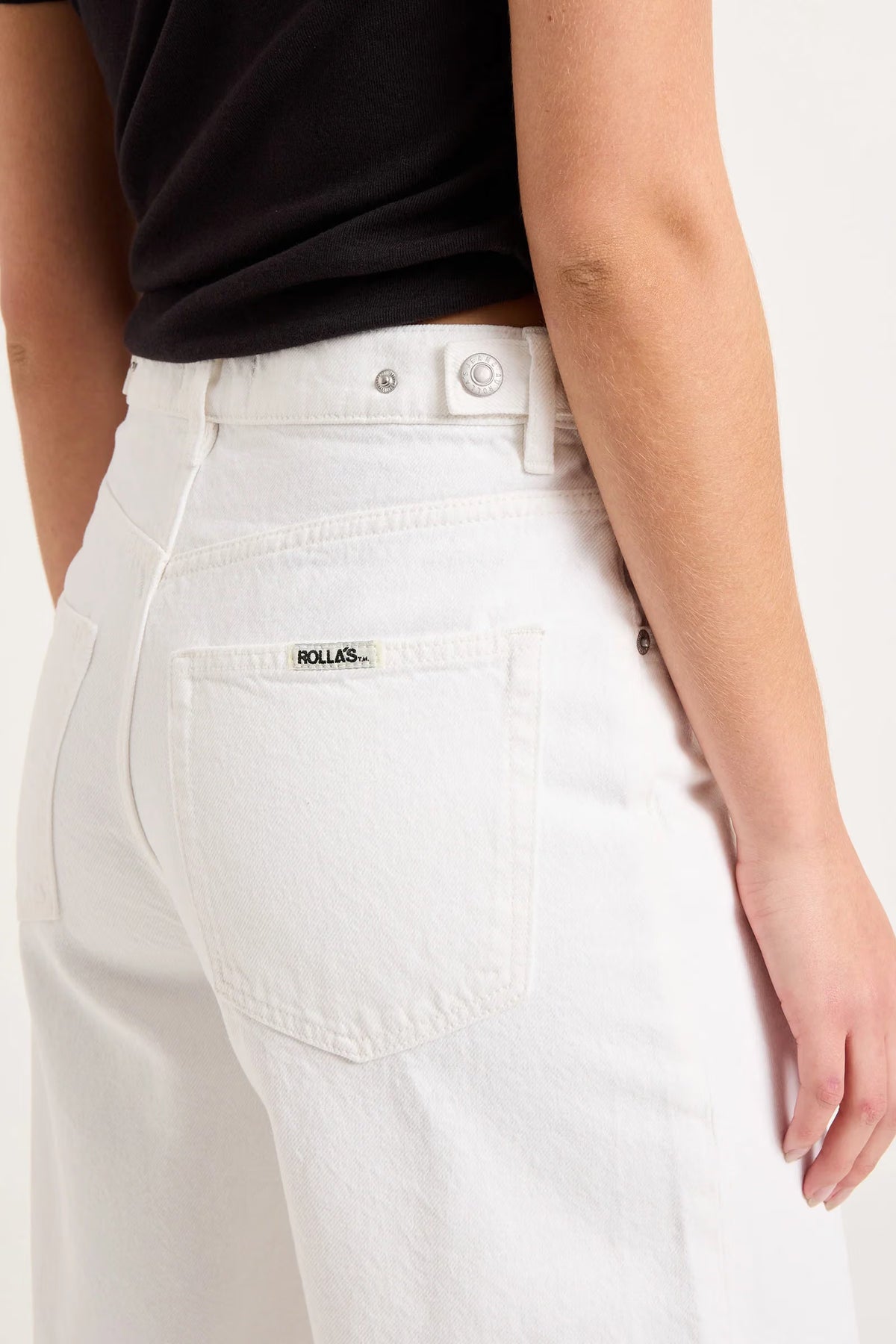 Close-up back view of white denim shorts showing the square back pocket, waistband and stitching.
