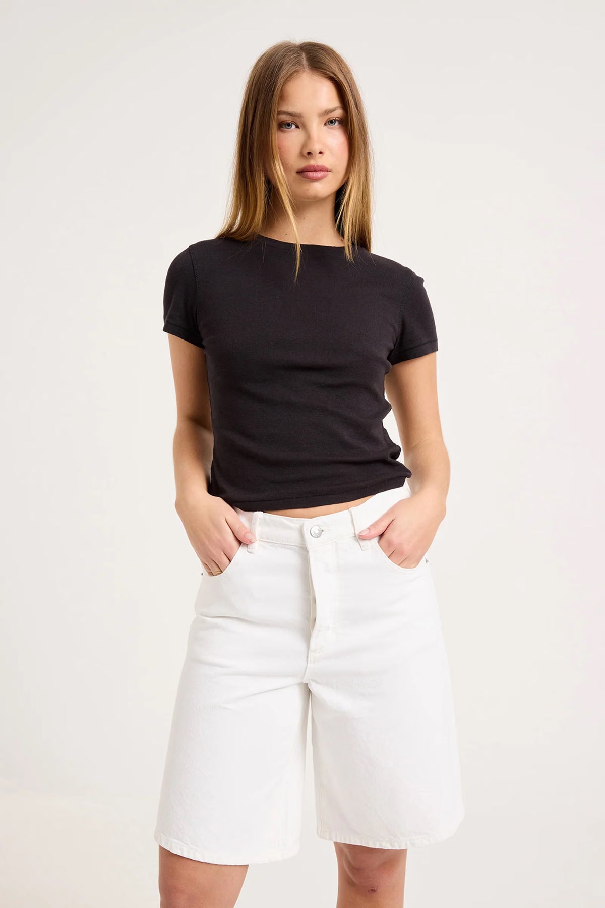 Close-up front view of white knee-length denim shorts showing the waistband, button closure, belt loops and front pockets.