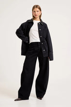 Model wearing the Mercer Black denim chore jacket over a white tee and black trousers, showing the button front, oversized sleeves, patch pockets and structured boxy silhouette in a full-length front view.