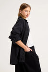 Close-up side view of the black denim chore jacket worn over a white tee, showing the contrast collar, dropped shoulder, rolled sleeve, washed denim texture and relaxed oversized fit.