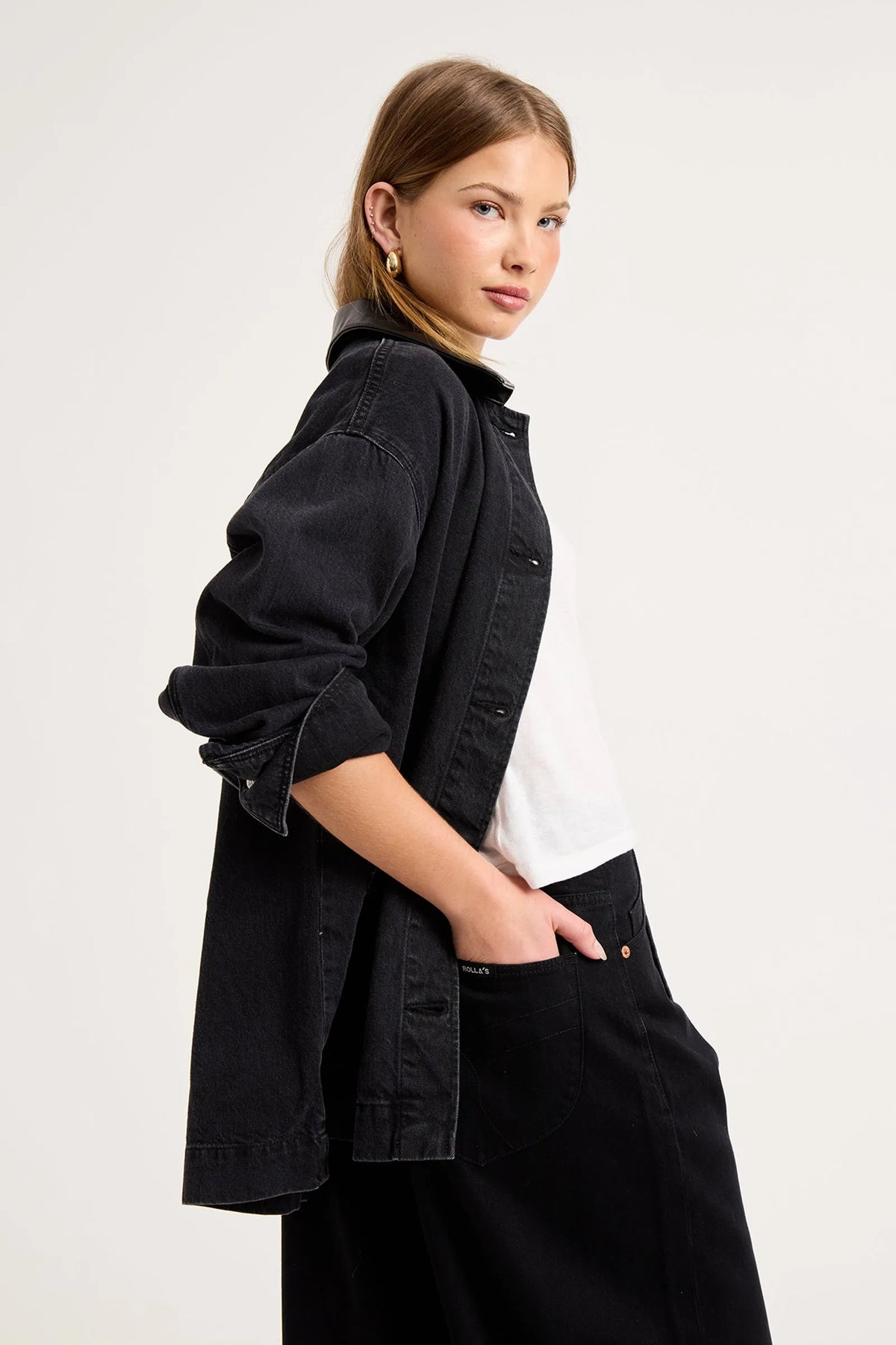 Close-up side view of the black denim chore jacket worn over a white tee, showing the contrast collar, dropped shoulder, rolled sleeve, washed denim texture and relaxed oversized fit.