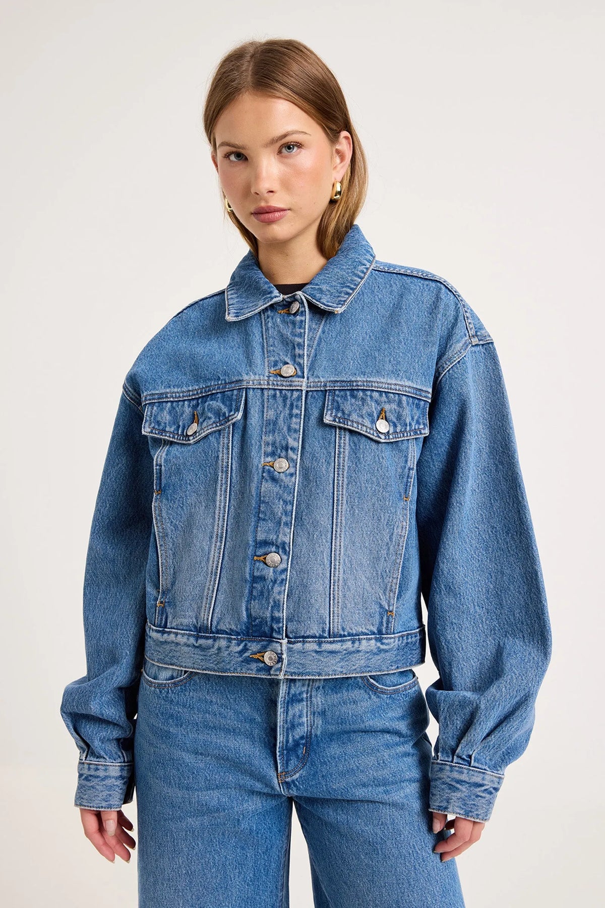 Model wearing the blue denim swing jacket with matching jeans, showing the pointed collar, structured chest pockets, silver buttons and relaxed cropped silhouette, front view
