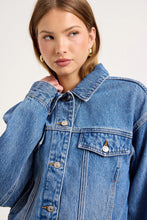 Close-up of a model wearing the Soho Vintage blue denim swing jacket, showing the pointed collar, silver button front, flap chest pocket, gold topstitching, dropped shoulders and oversized sleeve detail.