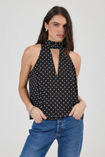 Woman wearing a black polka dot halter top and blue jeans on a white background