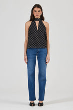 Woman wearing a black polka dot top and blue jeans on a white background